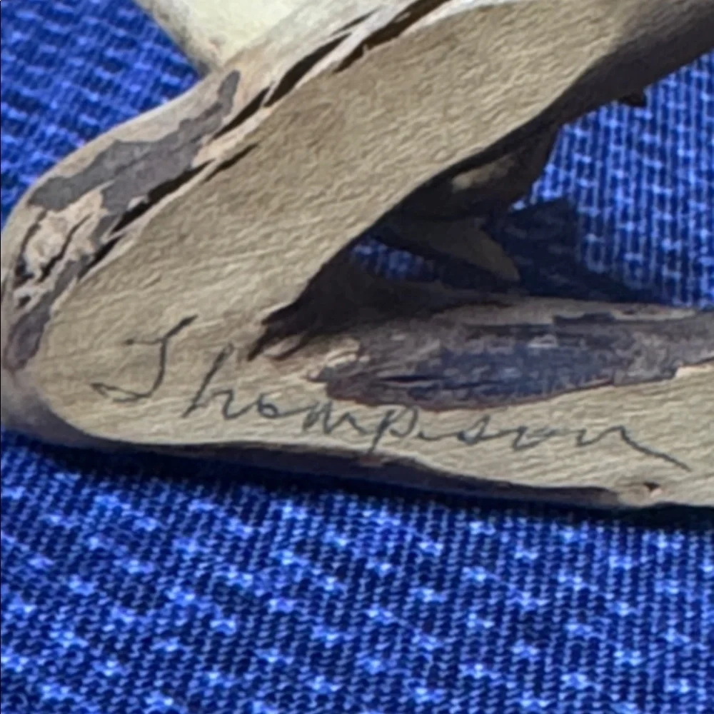 Hand carved wooden bird sculpture perched on a piece of natural wood signed